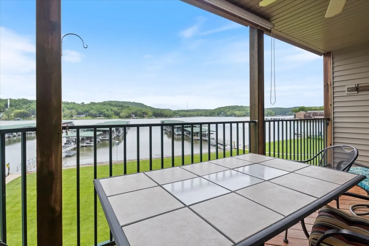 An inviting private deck with a stylish outdoor dining table set against the backdrop of a shimmering waterfront. The space is surrounded by a lush green lawn and offers a clear view of the docking area and the lake beyond, creating an ideal setting for outdoor meals, morning coffee, or evening gatherings.