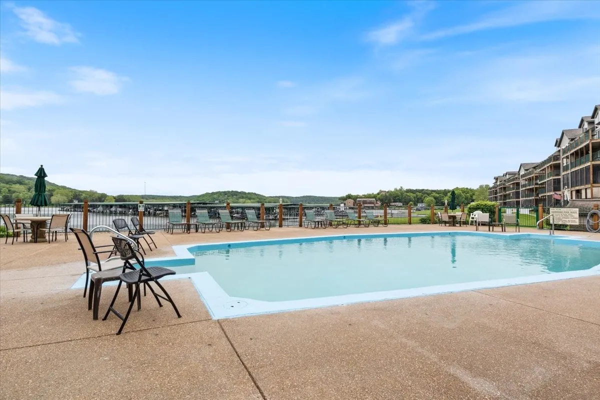The swimming pool area with surrounding lounge chairs and a picturesque view of the lake and wooded hills beyond. The scene is peaceful, with the pool just steps away from the deck, illustrating convenient access to resort-style amenities and lakeside relaxation.