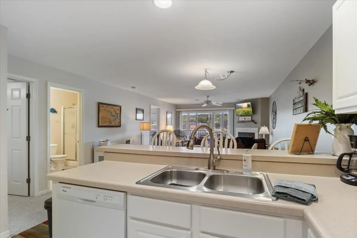 An open-concept interior showcasing the kitchen island, dining table, and a cozy living area, all seamlessly connected. Large windows in the background provide a view toward the pool and lake, filling the space with natural light. The kitchen is equipped for meal prep, while the dining area is ready for family gatherings. Comfortable furnishings invite relaxation.