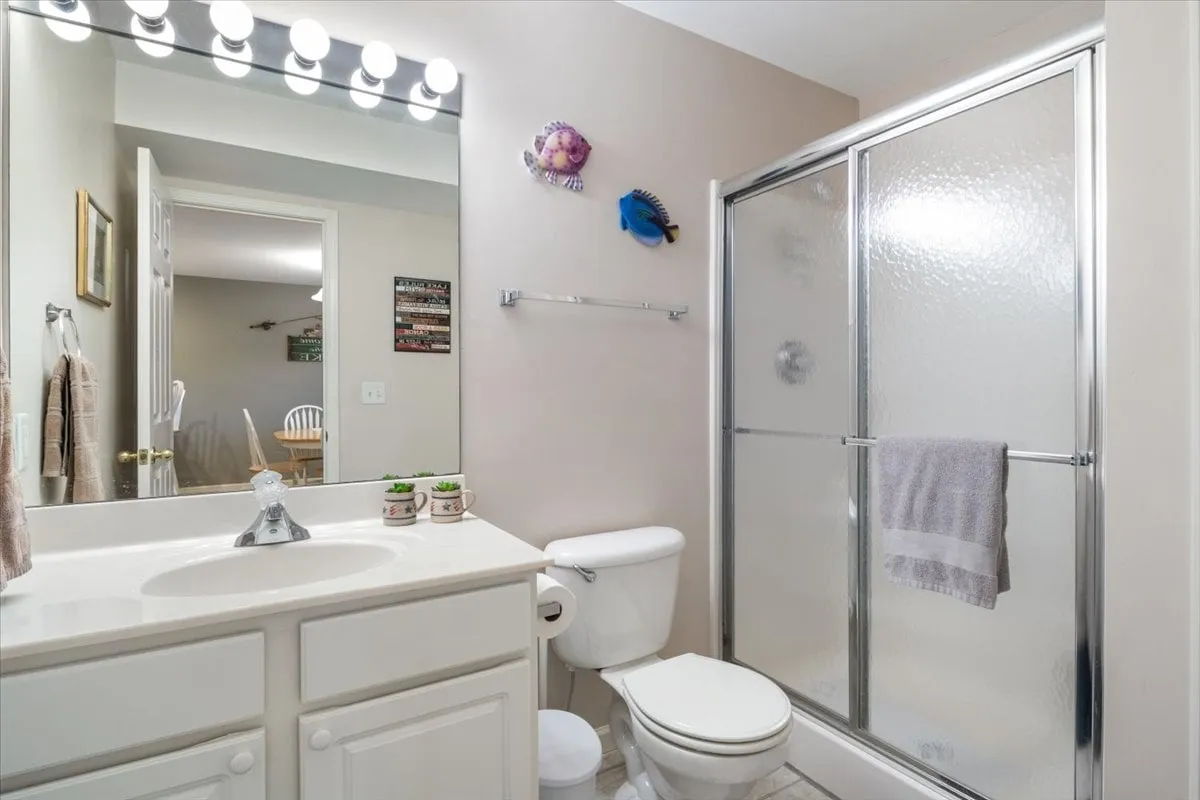 A bright bathroom with a modern vanity, a large mirror, a shower stall, and decorative wall art. The space is organized and welcoming, ideal for morning routines or a relaxing shower after a busy day.