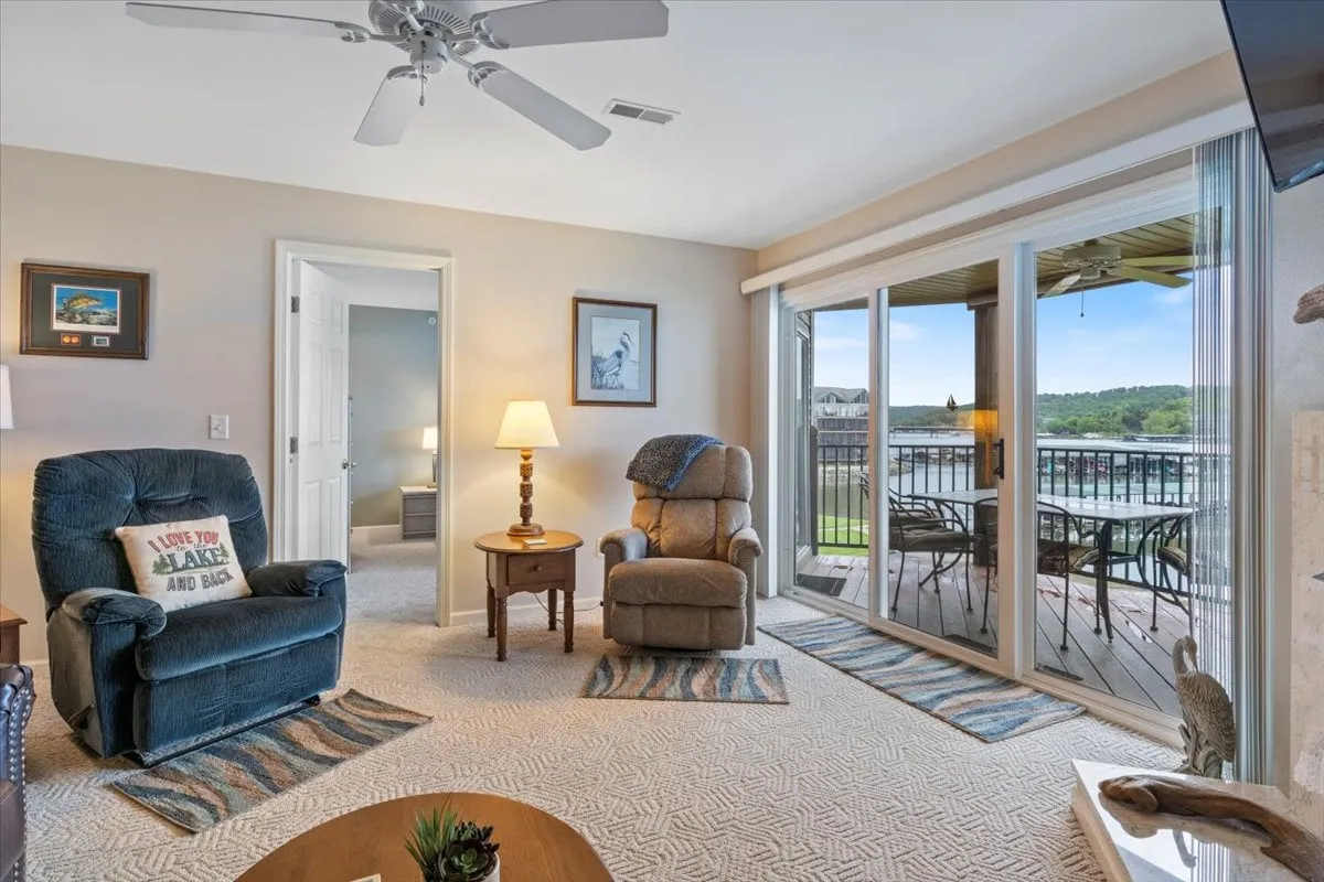 A comfortable seating area features a blue recliner and a tan armchair positioned near sliding glass doors that open onto a deck. The arrangement suggests easy access from the living space directly to the outdoors, with the deck likely offering views of the lake and proximity to community amenities like docks and slips.