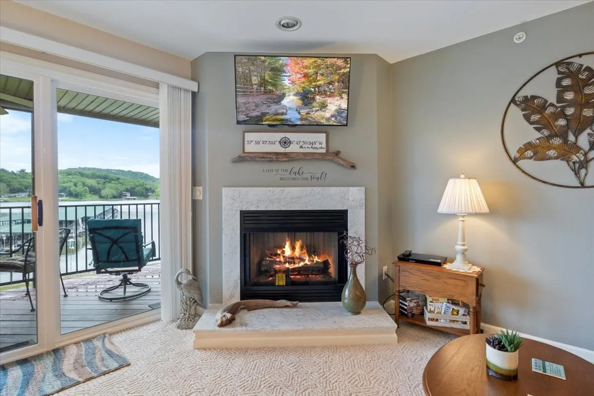 A cozy living area featuring a fireplace, a television displaying a nature scene, decorative wall art, and a reading table with a lamp. The ambiance is warm and welcoming, suggesting relaxation after a day spent exploring the area.