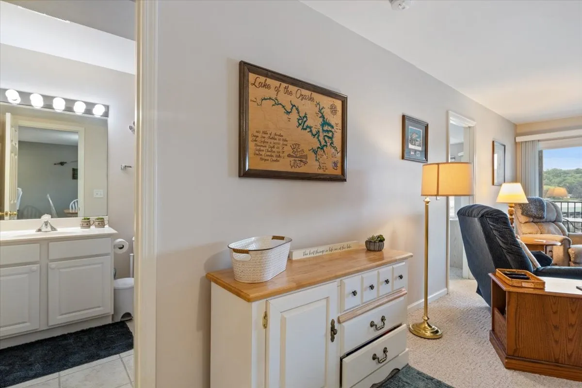 A cozy reading nook with a recliner chair, wooden dresser, and a framed map of the Lake of the Ozarks as the focal point. Soft lighting and a relaxed atmosphere suggest a space for planning or recounting the day's adventures on the water.