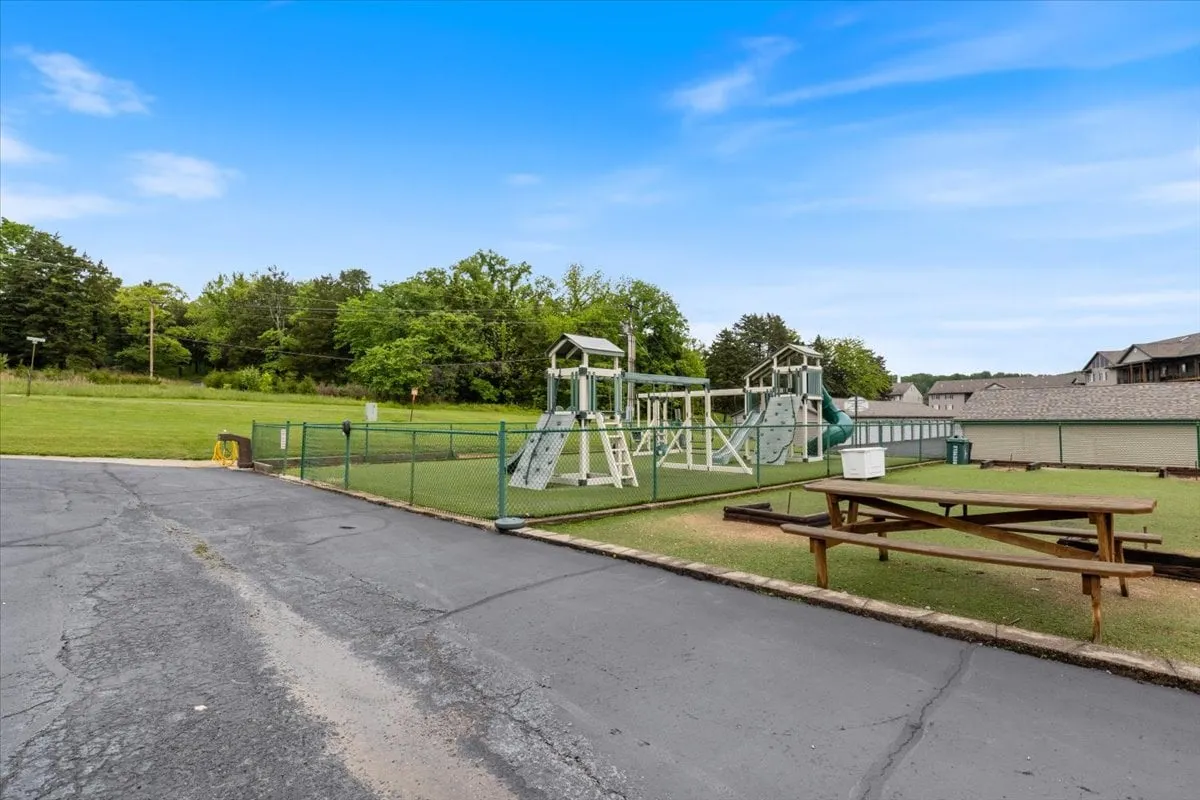 This exterior photo captures a lively playground with colorful equipment, picnic tables, and an open grassy area. Children can be seen playing, and families are gathered at picnic tables, all set within a secure and welcoming environment.